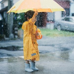 little girl in Toronto neighbourhood in rain with yellow raincoat, umbrella, and rain boots.